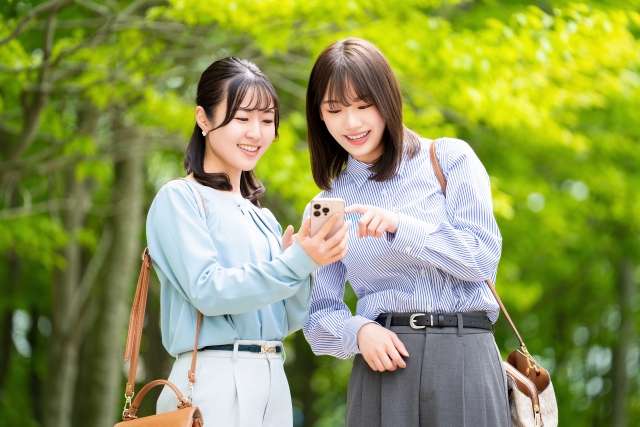 スマホを見ながら話す2人の女性、お出かけ、友達、旅行